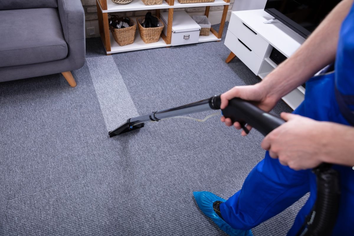 A man in a blue shirt is using a vacuum cleaner on a carpet, focusing on cleaning the floor.